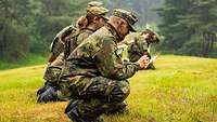 Mehrere Soldaten kniene auf einer Wiese und fertigen eine Skizze an.