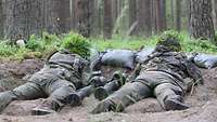 Soldaten liegen mit zwei Panzerfäusten zwischen sich in einer Stellung im Wald