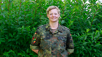 Eine Soldatin steht vor einer Hecke