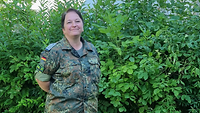Eine Soldatin steht vor einer Hecke