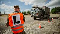 Rückansicht eines Soldaten in orangener Weste. Im Hintergrund ein Lkw der Bundeswehr.