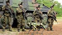 Vier bewaffnete Soldaten stehen vor einem Panzer. Vor ihnen steht ein Roboterhund.