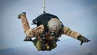 Ein Soldat fliegt mit einem großen Rucksack und einer Sauerstoffmaske im Gesicht.