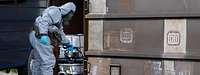 Ein Mensch in Schutzanzug hält ein Gerät an einen Eisenbahnwaggon