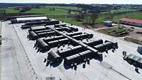 Luftaufnahme einer militärischen Zeltstadt. Im Hintergrund ländliche Szenerie.