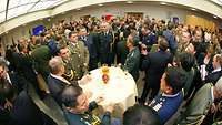 Ein Stehempfang mit vielen Menschen. Im Vordergrund ein Stehtisch mit internationalen Soldaten.
