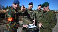 Soldaten in unterschiedlichen Uniformen besprechen sich auf einer Gleisanlage.