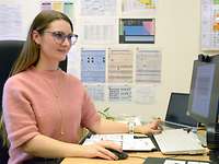Maria H. am Schreibtisch Eine Frau mit Brille und langen braunen Haaren sitzt an einem Schreibtisch und arbeitet an einem PC.
