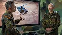 Ein Soldat spricht mit einem Soldaten stehend an einem Tisch vor einem Monitor