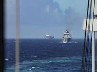 Bild von zwei Schiffen, vorderes Schiff ein graues Kriegsschiff, dahinter ein Containerschiff