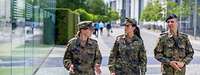Ein Soldat und zwei Soldatinnen in Flecktarnuniformen laufen nebeneinander. Sie sind im Gespräch.