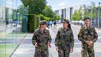 Ein Soldat und zwei Soldatinnen in Flecktarnuniformen laufen nebeneinander. Sie sind im Gespräch.