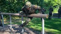 Ein Soldat überwindet einen Schwebebalken auf der Hindernisbahn, während Kameraden zusehen.