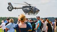 Zuschauer beobachten einen Hubschrauber vom Typ H145M LUH SOF im Tiefflug während einer Flugshow