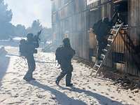 Bewaffnete Soldaten dringen über eine Leiter durch ein Fenster in ein Holzgebäude ein