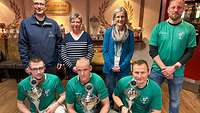 Drei Männer halten beim Gruppenfoto nach einer Siegerehrung Pokale in der Hand