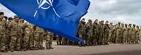 Soldaten verschiedener Nationen sind angetreten. Im Vordergrund wehen die Flaggen der EU und NATO.