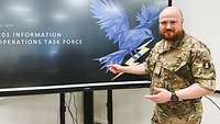 Ein Soldat steht vor einem großen Bildschirm.