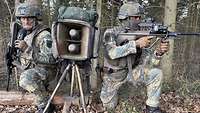 Zwei Soldaten knien im Wald neben einer Lautsprecheranlage.