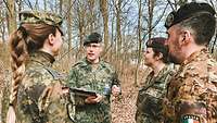 Vier Soldatinnen und Soldaten verschiedener Nationen stehen in einem Waldstück zusammen.