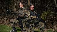 Zwei Soldaten knien vor einem Wald. Einer hält einer Drohne in der Hand.