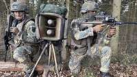 Zwei Soldaten knien im Wald zwischen einem Lautsprecher.