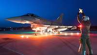 Ein Eurofighter steht beleuchtet auf der „Platte“. Ein Soldat gibt Lichtzeichen.