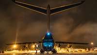 Ein Transportflugzeug steht bei Nacht mit offener Heckrampe auf einem Flugfeld.