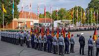 Auf einem Platz stehen angetretene Soldaten, im Hintergrund wehen die Flaggen der 16 Bundesländer. 