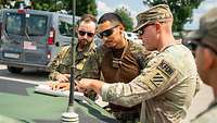 Deutsche und amerikanische Soldaten stehen an einem Fahrzeug und schauen auf eine Karte