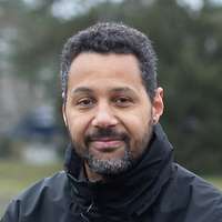 Ein Mann und eine Frau sitzen auf der Rückenlehne einer Bank. Im Hintergrund ist ein Teich zu sehen.