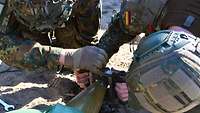 Zwei Soldaten beugen sich über ein Geschoss und bringen ein rahmenförmiges Gerät an.