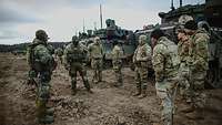 Deutsche und amerikanische Soldaten stehen vor Fahrzeugen im Gelände und sprechen miteinander.