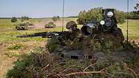 Zwei Soldaten auf einem Waffenträger Wiesel im Gelände, im Hintergrund fahren zwei Panzer