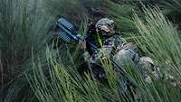 Zwei Soldaten knien in hohem Gras. Einer hält einen Sensor in der Hand.
