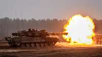 Ein Kampfpanzer mit starkem Mündungsblitz während der Schussabgabe.