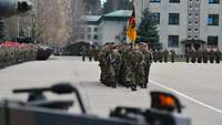 Soldiers stand in formation in a square. A delegation marches with a troop flag.