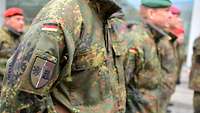Soldiers stand in formation during a roll call. There is a patch with the coat of arms on one sleeve.