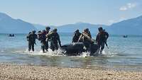 Vor bayerischen Bergen stürmen Soldaten aus einem Schlauchboot an ein Seeufer