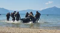 Vor bayerischen Bergen stürmen Soldaten aus einem Schlauchboot an ein Seeufer