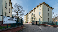 Beige Gebäude vor blauem Himmel, im Vordergrund befinden sich Hinweisschilder
