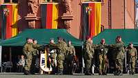 Menschen in Uniformen stehen vor einem Gebäude mit der Landesflagge von Rheinland-Pfalz