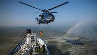 Ein Bundespolizei-Hubschrauber mit einer Person am Seil schwebt über einem Boot im Meer