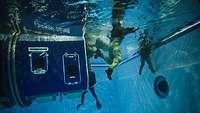 Personen verlassen eine Hubschrauberkabine unter Wasser in einem Schwimmbecken