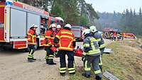 Feuerwehrleute tragen eine Verletzte Person. Im Hintergrund stehen verschiedene Feuerwehrautos