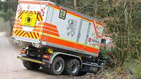 Ein weiß-signalfarbener Transporter steht schräg hangabwärts in ein Waldstück hinein.