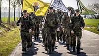 Soldaten in Marschformation tragen drei Flaggen.