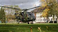Ein Militärhubschrauber landet auf einer Wiese vor einem Gebäude