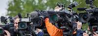 Journalisten stehen mit ihren Kameras und ihren Stativen nebeneinander. Alle Objektive schauen in eine Richtung.