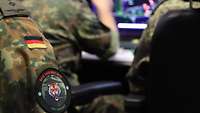 Mehrere Soldaten sitzen vor einem Monitor. An einem Ärmel ist ein Patch zu sehen.